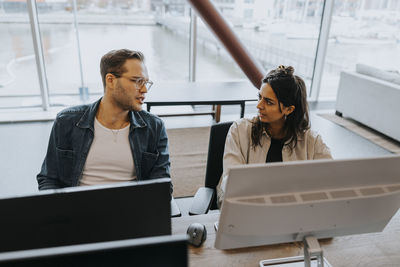 Young male and female business colleagues discussing while sitting at computer desk in office