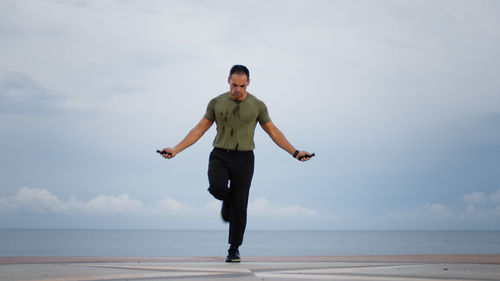 Man warm up jump rope against the ocean during cloudy day