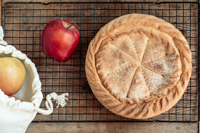 Round apple pie on a wooden background with fresh apples in a canvas bag
