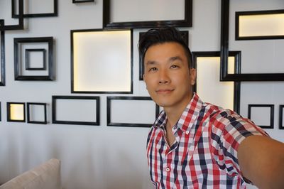 Portrait of man standing against frames on wall