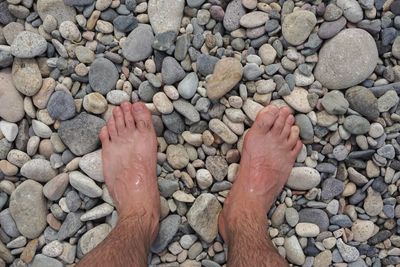 Low section of man standing on pebbles