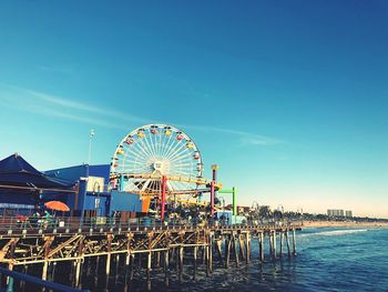 Ferris wheel by sea against clear blue sky