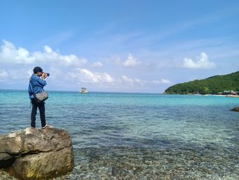 Man standing on rock by sea against sky