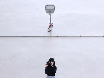 Young woman photographing against wall