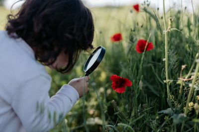 Rear view of girl looking at flower through magnifying glass