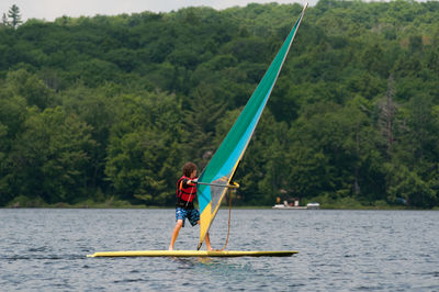 Teenage boy paddleboarding on river against trees