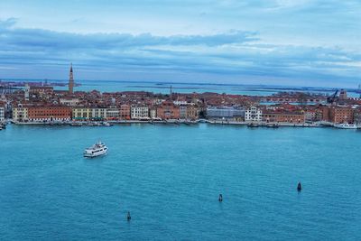 Sailboats in sea by buildings against sky