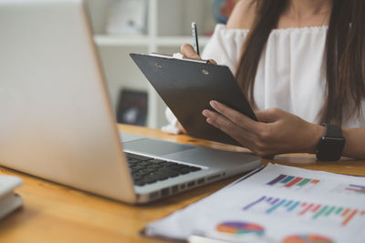 Midsection of woman reading book while sitting on table
