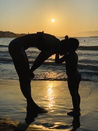 Silhouette people standing on beach against sky during sunset