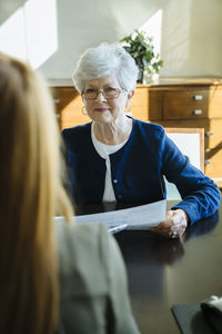 Senior woman holding documents while discussing with financial advisor in office