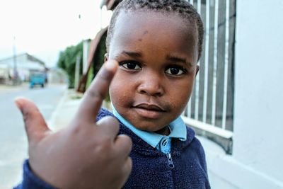 Close-up portrait of boy pointing while standing on footpath