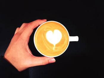 Cropped hand of woman holding cappuccino on black background