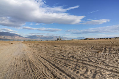 Tire tracks on desert land against sky