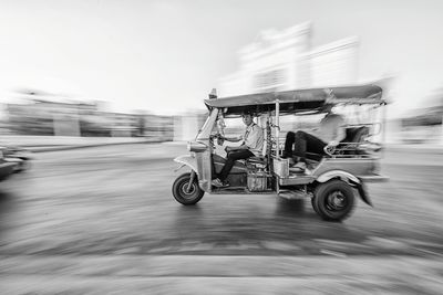 Blurred motion of men in jinrikisha on road against sky