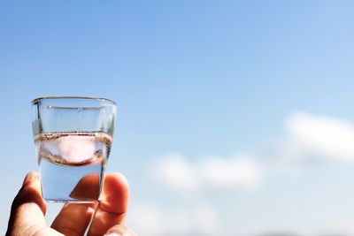 Close-up of hand holding drink against blue sky glass in the sky