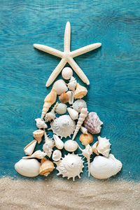 Christmas tree made from sea shells and starfish on wooden blue background, top view