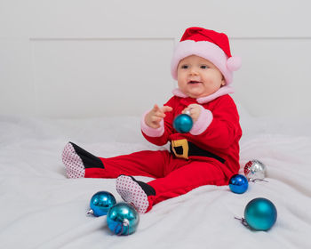 Full length of cute baby sitting on bed playing with bauble