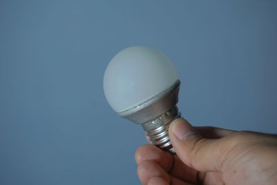 Close-up of hand holding light bulb against blue background