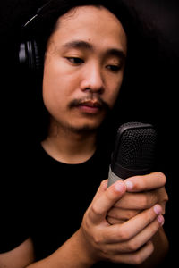 Close-up of young singer holding microphone against black background