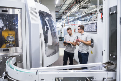 Two men talking at machine in factory shop floor