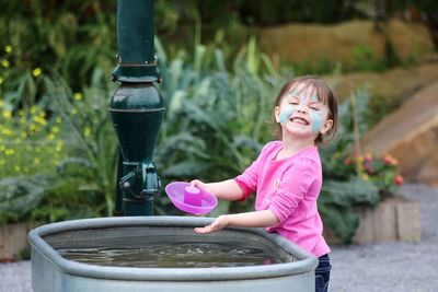 Portrait of cute smiling girl with face paint standing by water container