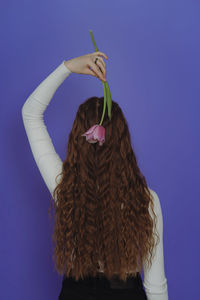 Portrait of young girl with long hair and tulip flower, standing with her back