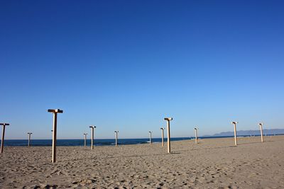 Wooden posts on beach against clear blue sky