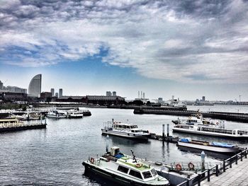 Boats in harbor against cloudy sky