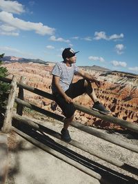 Young man sitting on railing against mountain