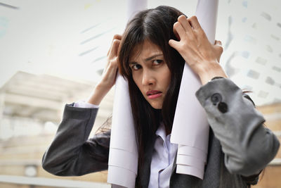 Portrait of stressed businesswoman with rolled papers in city