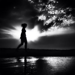 Silhouette of woman standing by sea against cloudy sky