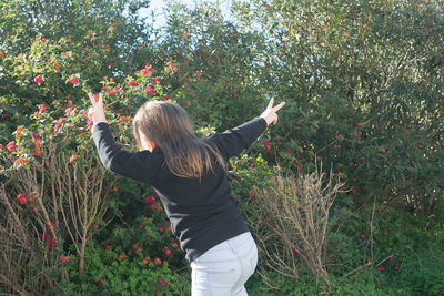 Rear view of girl showing peace sign while running against plants at park