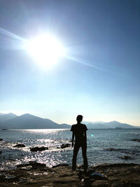 Man standing on beach against sky on sunny day