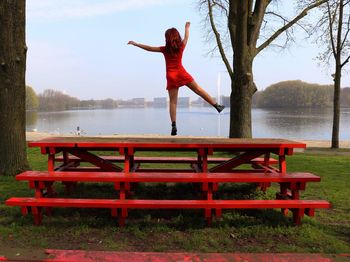 Full length of woman walking on bench by tree against sky