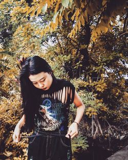 Young woman standing by tree during autumn