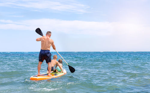 A father and two children ride a sup board on the sea, sail towards the horizon. paddleboarding.