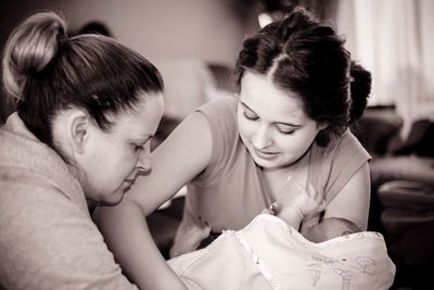 Mother giving newborn baby boy to daughter at home