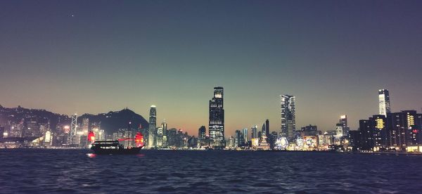 Illuminated modern buildings in city against clear sky