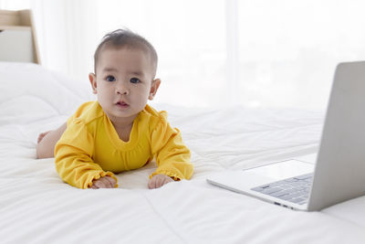 Portrait of cute girl using laptop on bed at home