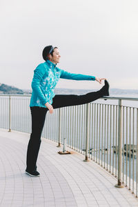 Mid adult woman stretching on promenade against clear sky