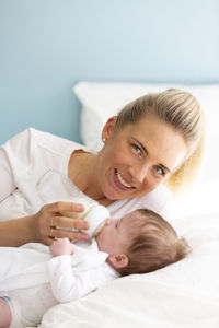 Portrait of smiling mother feeding milk to daughter on bed at home