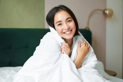 Portrait of young woman sitting on bed at home