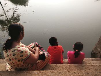 Rear view of people sitting by lake