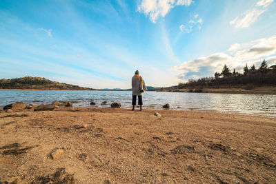 Rear view of woman standing on shore at beach against sky