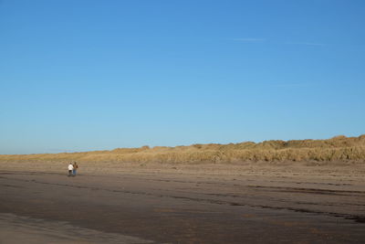 Man walking on desert against clear blue sky