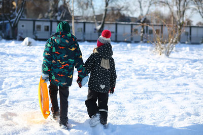 Winter portrait of children with a plastic sled walking on snow and holding hands
