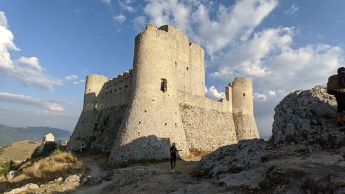 Low angle view of woman standing by building against sky