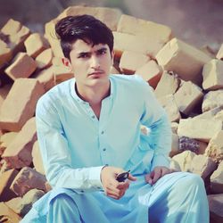 Portrait of serious young man wearing kurta while sitting on rocks