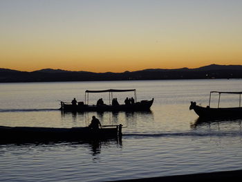 Silhouette people in boat on lake against sky during sunset
