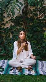 Full length of young woman meditating while sitting outdoors